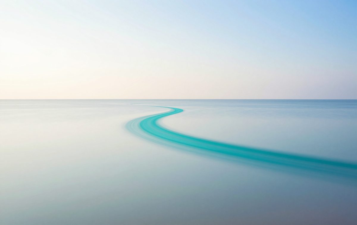 A rising trail of turquoise light above calm water